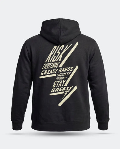 A black pullover hoodie shown from the back, featuring a large cream-colored graphic print with the text 'RISK EVERYTHING - GREASY HANDS SOCIETY - STAY GREASY' and diagonal lightning-bolt shapes, on a light gray background - Bolted Down Black Hoodie by Greasy Hands Society