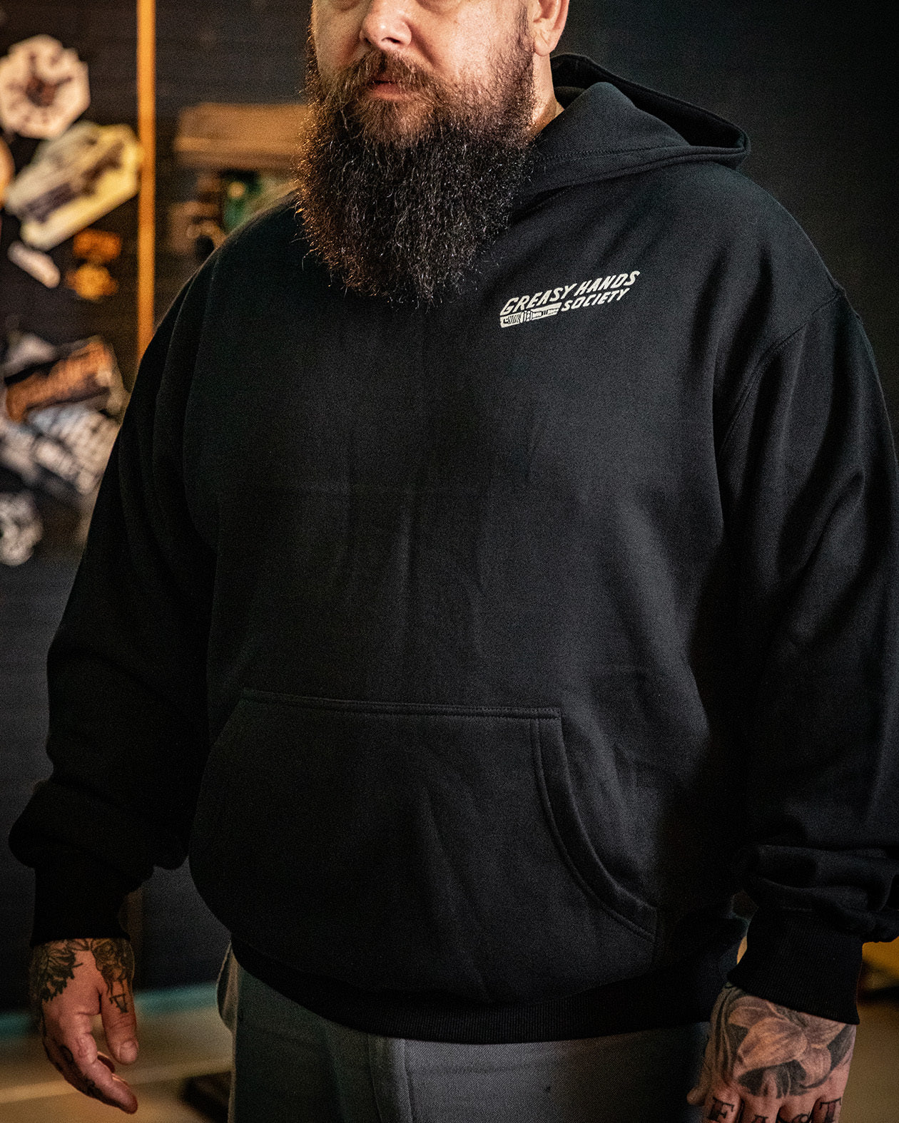bolted down black heavyweight box hoodies front view on a model showing greasy hands society, and a screw on the front left chest - Bolted Down Men's Black Hoodie by Greasy Hands Society