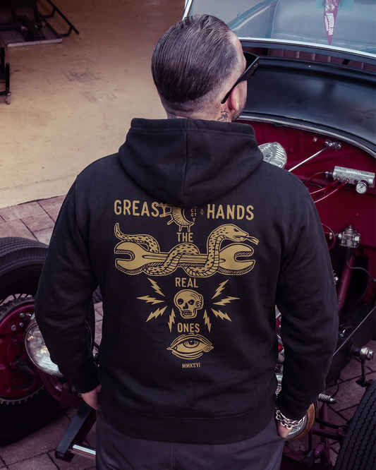 A man viewed from behind wearing a black hoodie with a large gold graphic print on the back, standing next to a classic red car in a garage - Snake Eye Hoodie by Greasy Hands Society