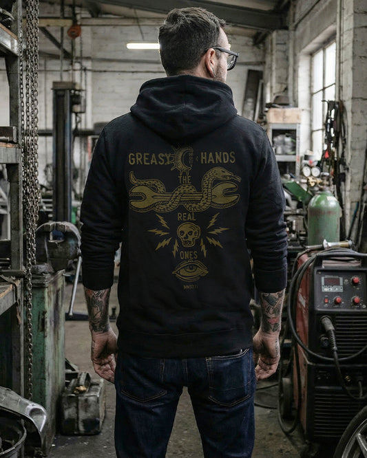 Person wearing a black hoodie from greasy hands society called the snake eyes hoodie with a snake and wrench graphic design in a workshop setting