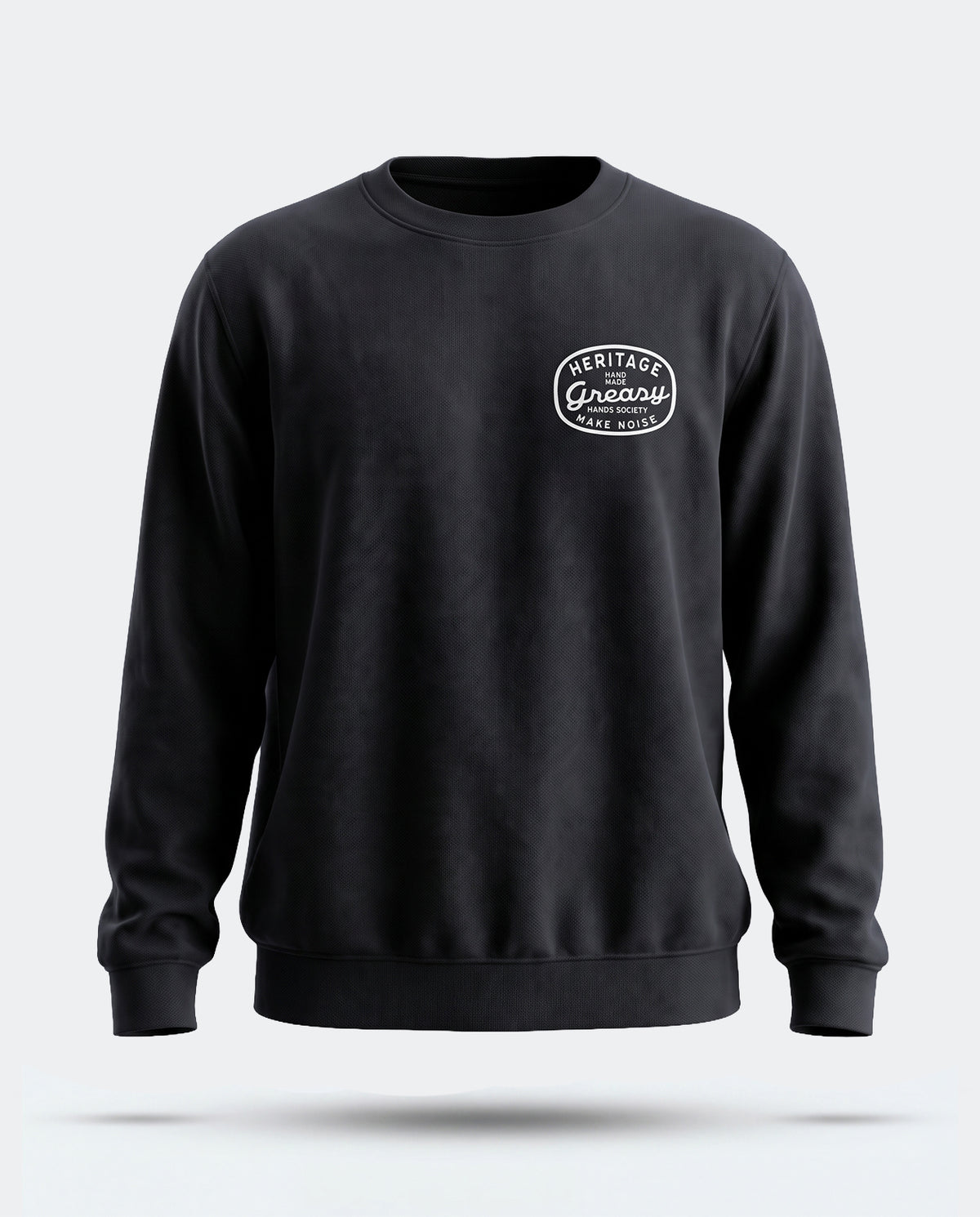 A black crewneck sweatshirt with a white circular 'Heritage - Greasy Hands Society' logo on the left chest, displayed on a light gray background with a soft shadow underneath - The Heritage Sweatshirt by Greasy Hands Society