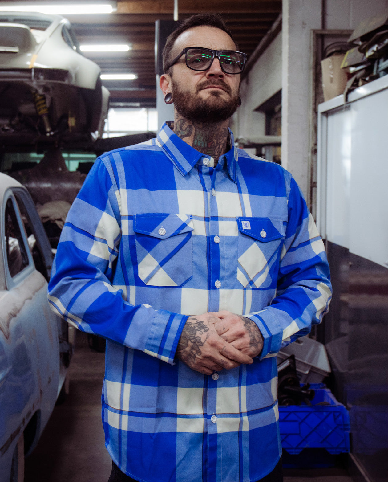 Man wearing a plaid blue and white flannel shirt in a garage setting - the F**kin' Problems Flannel from Greasy Hands Society