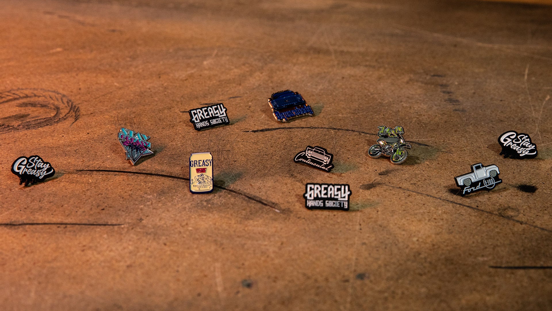 Collection of Greasy hands society brand enamel pins on a wooden surface