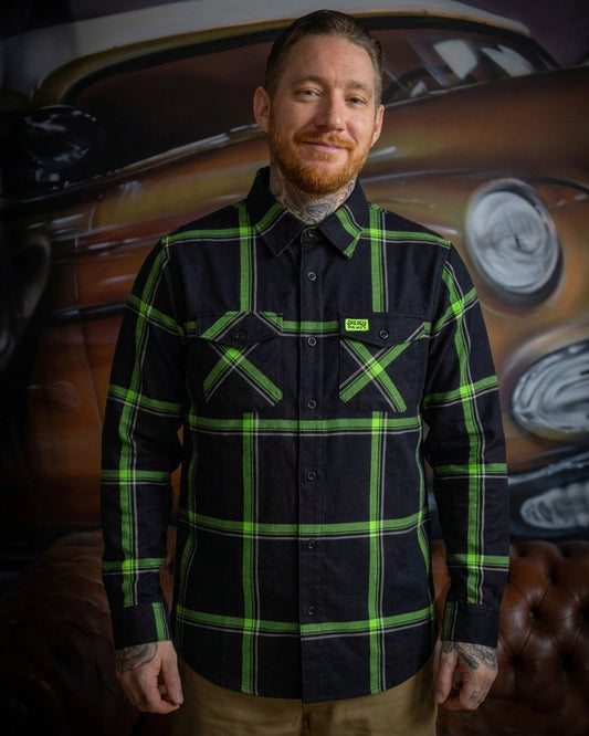Man wearing a black and green plaid flannel shirt with a vintage car in the background - The Moto Flannel by Greasy Hands Society