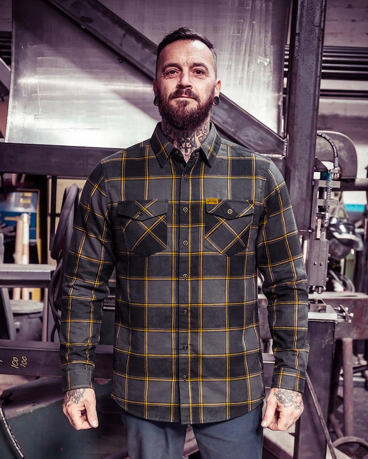 Man wearing a plaid gray and orange flannel shirt in an industrial setting - El Lobo Flannel by Greasy Hands Society