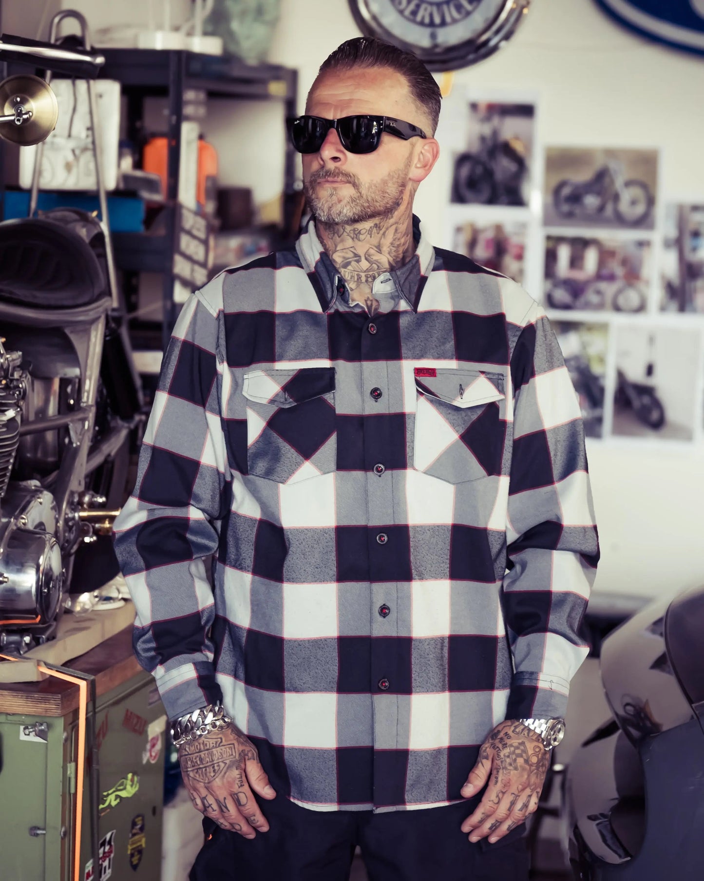 Man wearing a checkered black, gray and red flannel shirt in a room with motorcycles and decor - The Banger Flannel by Greasy Hands Society