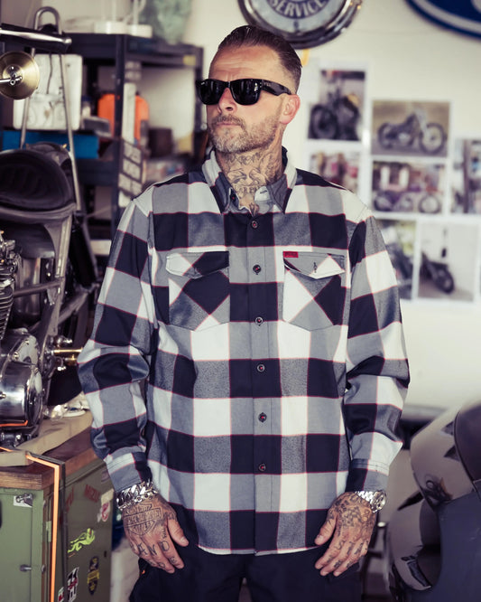 Man wearing a checkered black, gray and red flannel shirt in a room with motorcycles and decor - The Banger Flannel by Greasy Hands Society
