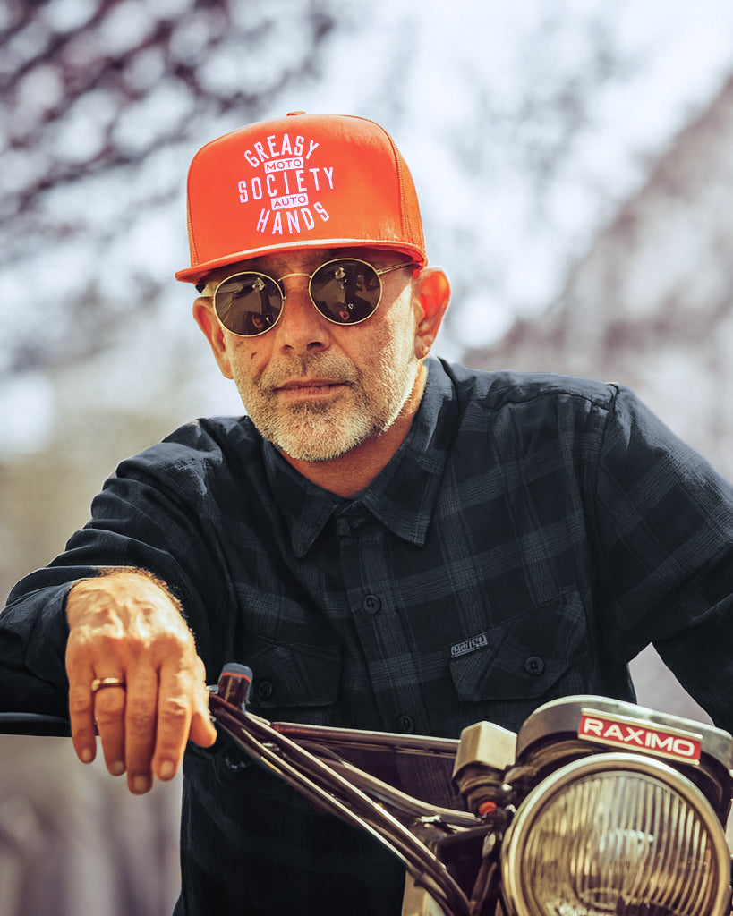 orange station hat greasy hands society hat being worn by a man on a motorcycle