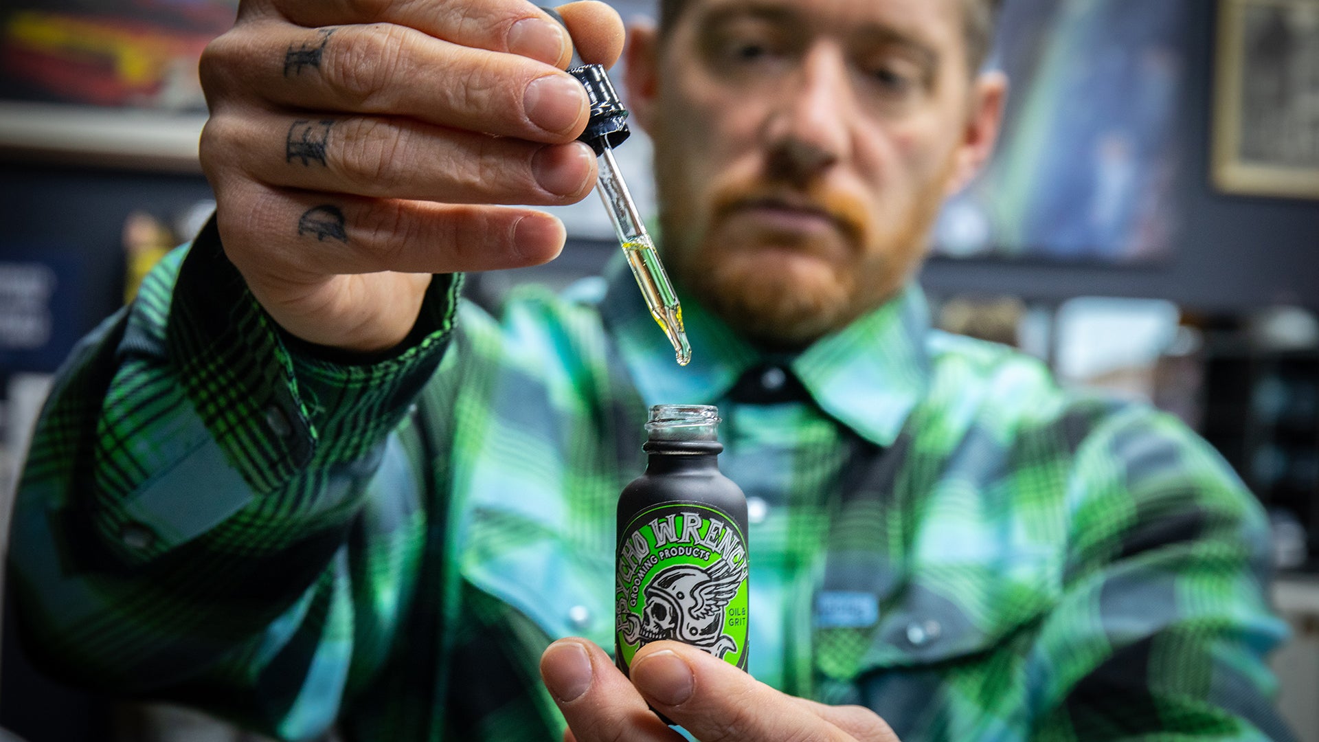 Person holding a bottle and dropper, possibly in an indoor setting. psycho wrench grooming products oil & grit scent tattoo oil