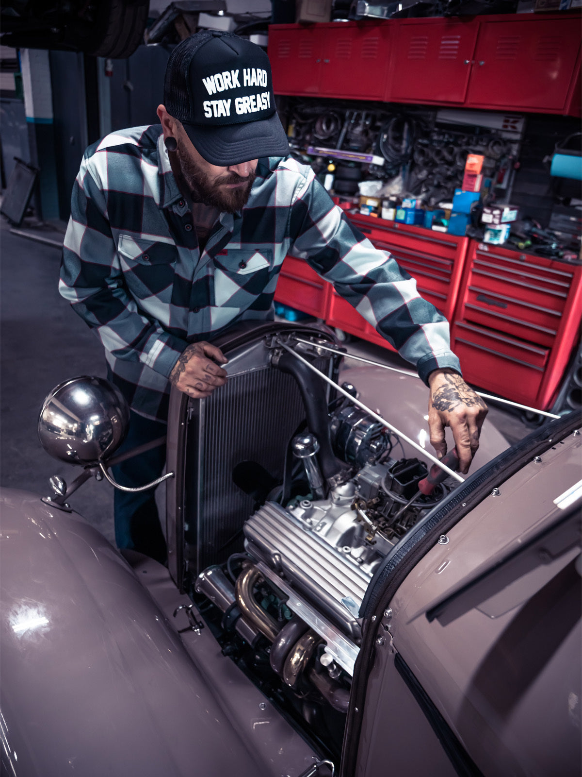 Person wearing a black and gray with small red line working on a car engine in a garage with a 'Work Hard Stay Great' cap - The Banger Flannel by Greasy Hands Society