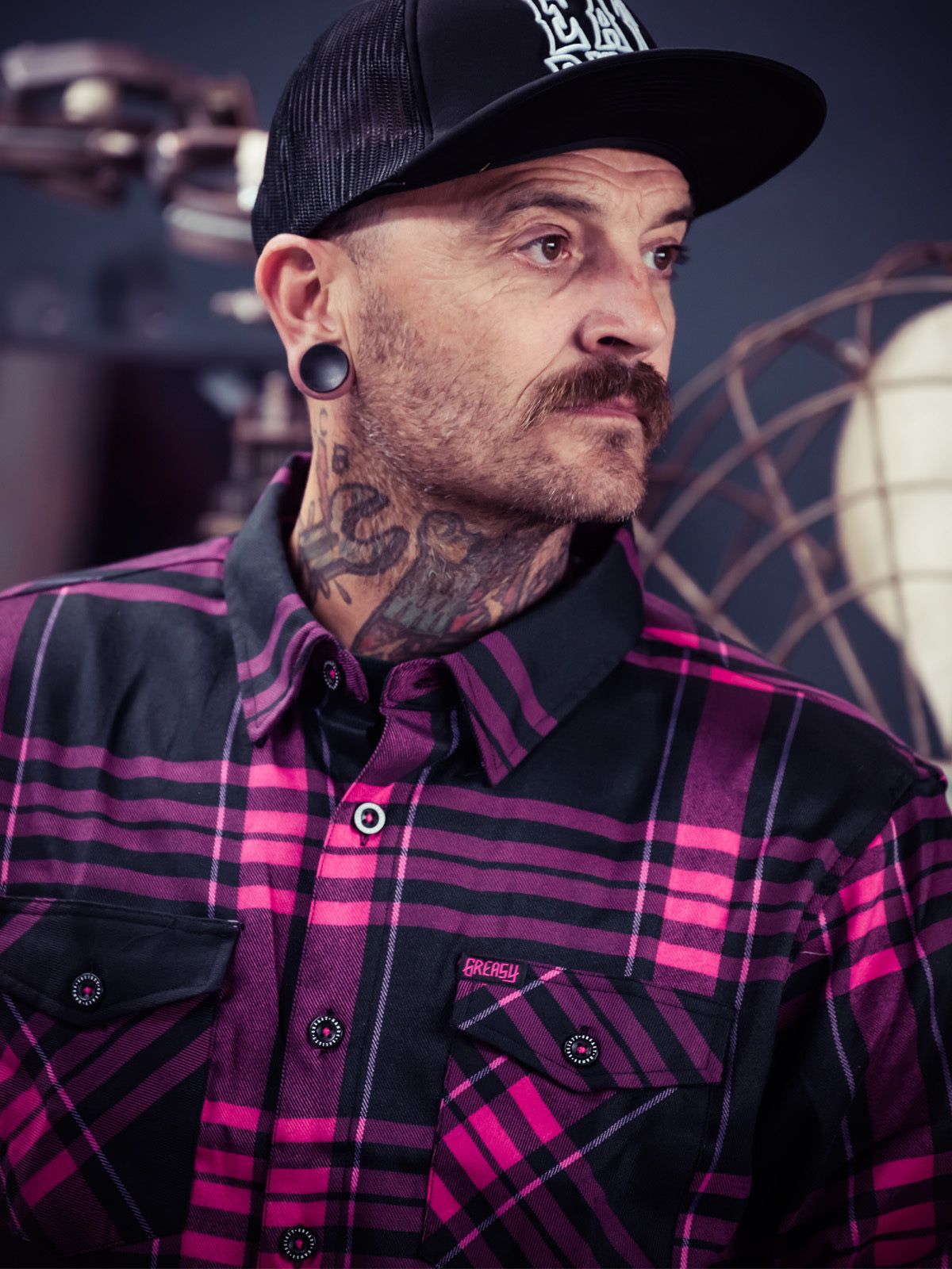 Man wearing a black and pink plaid shirt with a blurred background - Lonely Heart Flannel by Greasy Hands Society
