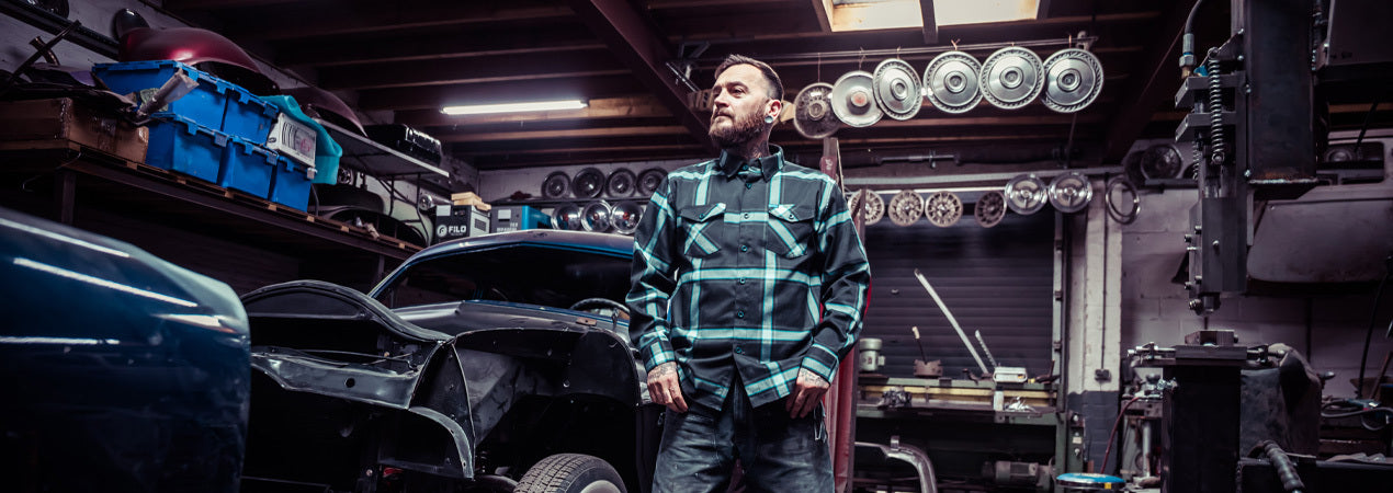 Person wearing a black and blue flannel plaid shirt in a garage setting for classic cars - Gravity Fed Flannel by Greasy Hands Society