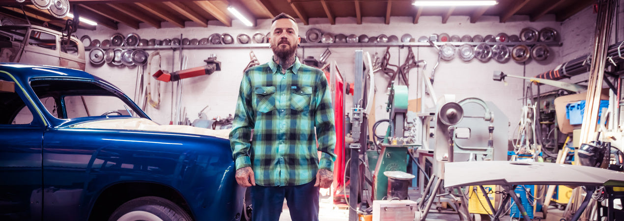 Man standing in a workshop with tools and a vintage car - The Sucker Punch Flannel by Greasy Hands Society