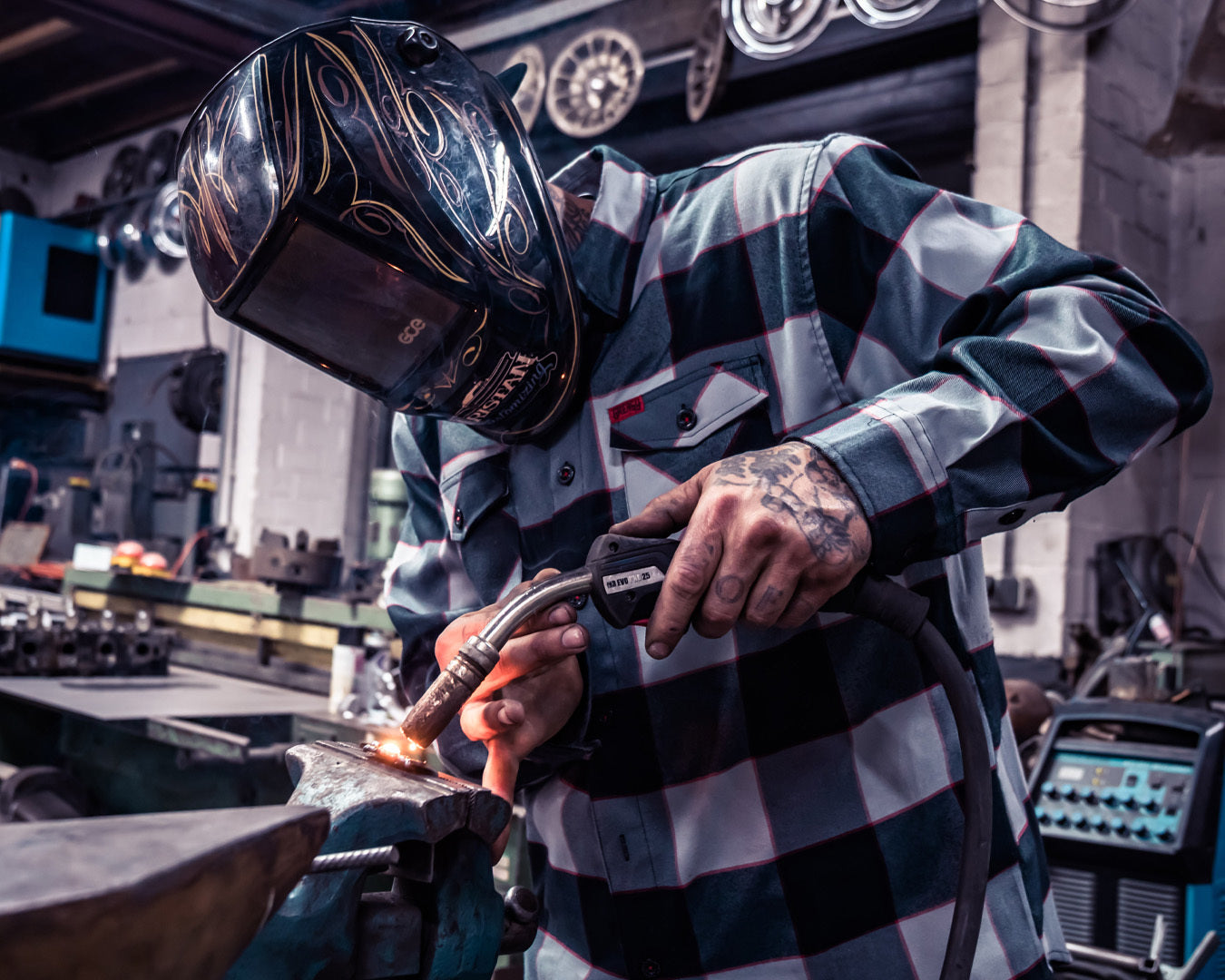 Person wearing a welding helmet and plaid black and gray shirt in a workshop setting - The Banger Flannel by Greasy Hands Society