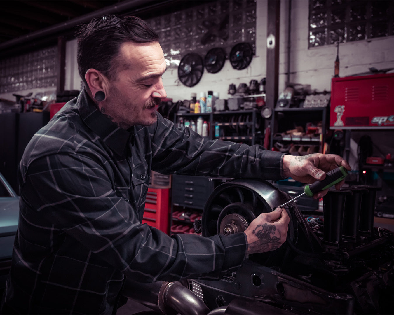 Person wearing a gray flannel shirt working on a car engine in a garage - The Dapper Flannel by Greasy Hands Society