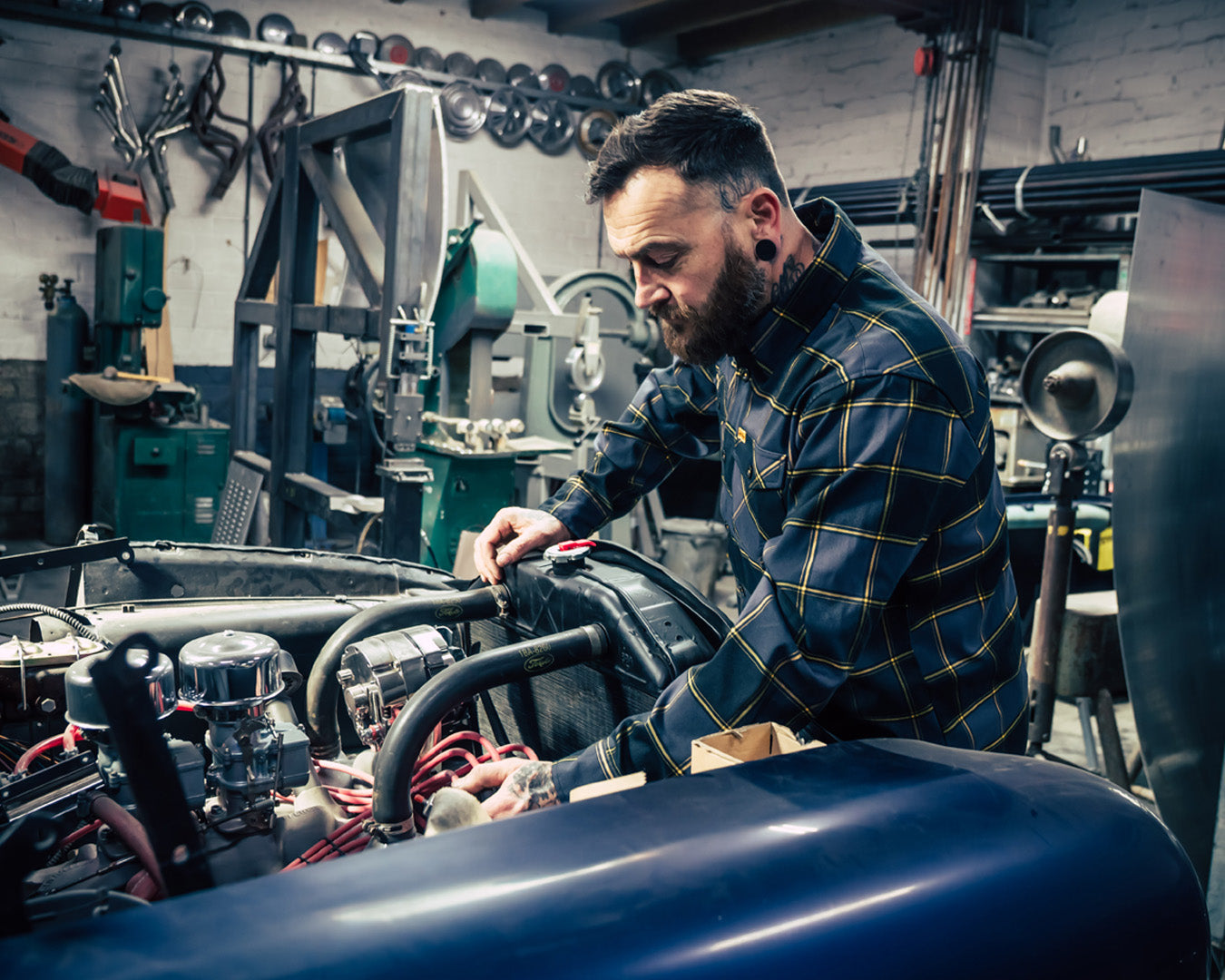 Man wearing a black, gray and orange flannel shirt working on a vehicle engine in a workshop - El Lobo Flannel by Greasy Hands Society