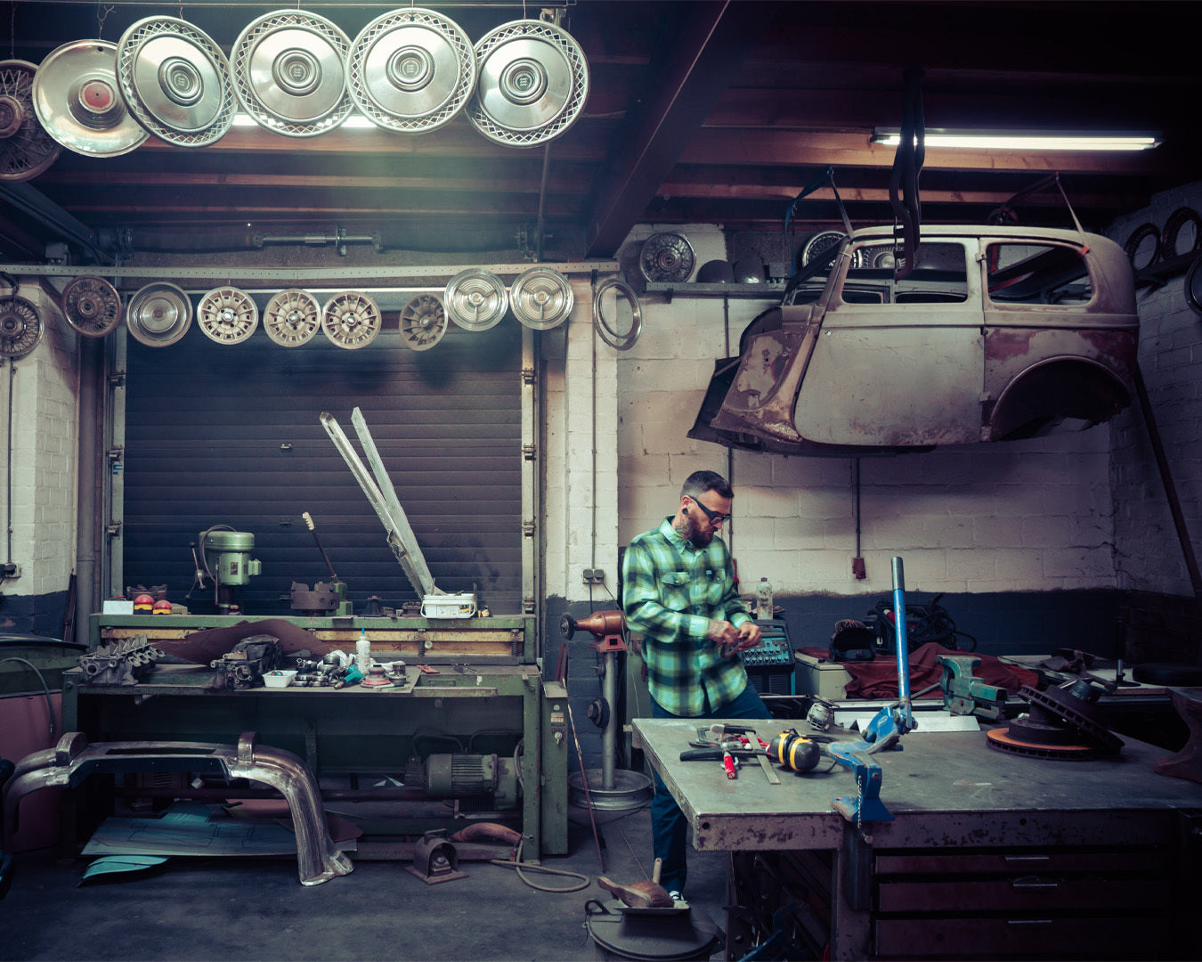 Person wearing a blue and green flannel shirt working in a workshop with tools and car parts around - The Sucker Punch Flannel by Greasy Hands Society