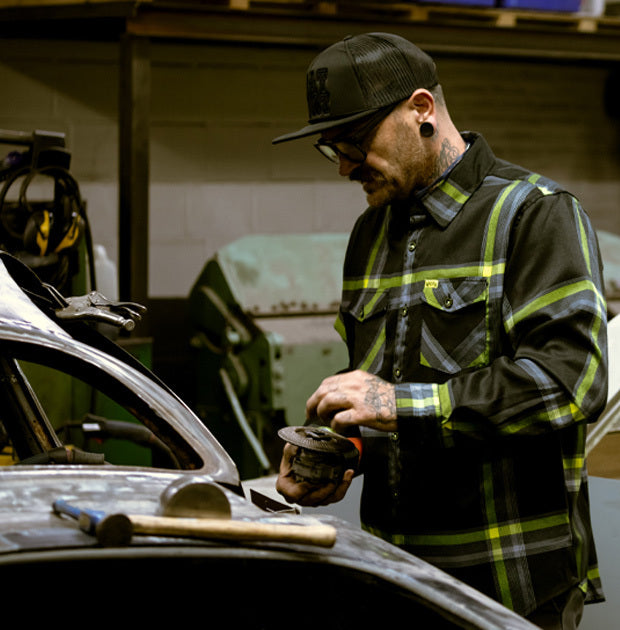 Man wearing a black and yellow plaid shirt working on a car in a garage - Eat Dust Flannel by Greasy Hands Society