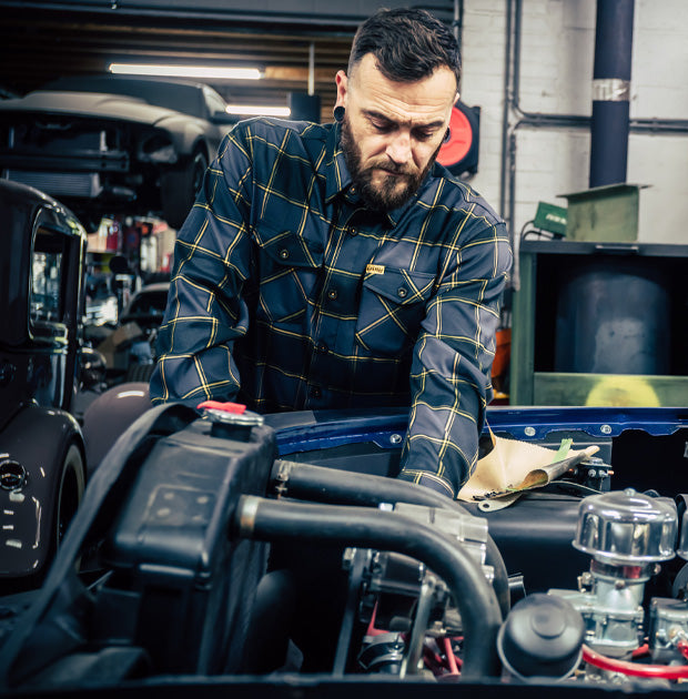 Mechanic wearing a black, gray and orange plaid flannel shirt working on a car engine in a garage - El Lobo Flannel by Greasy Hands Society
