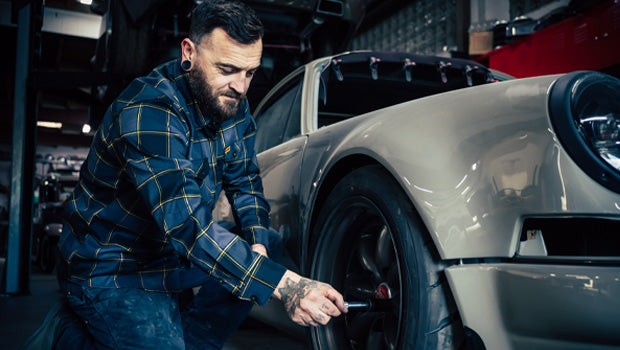 Man wearing a gray black and orange flannel shirt while working on a car tire in a garage - El Lobo Flannel by Greasy Hands Society