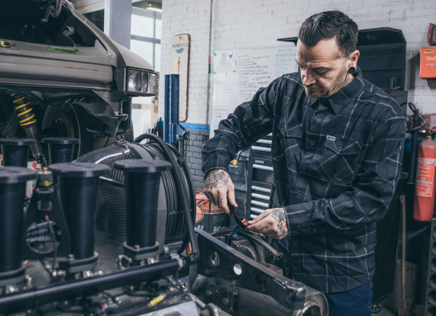 Mechanic wearing a gray flannel shirt working on a vehicle engine in a garage - The Dapper Flannel by Greasy Hands Society