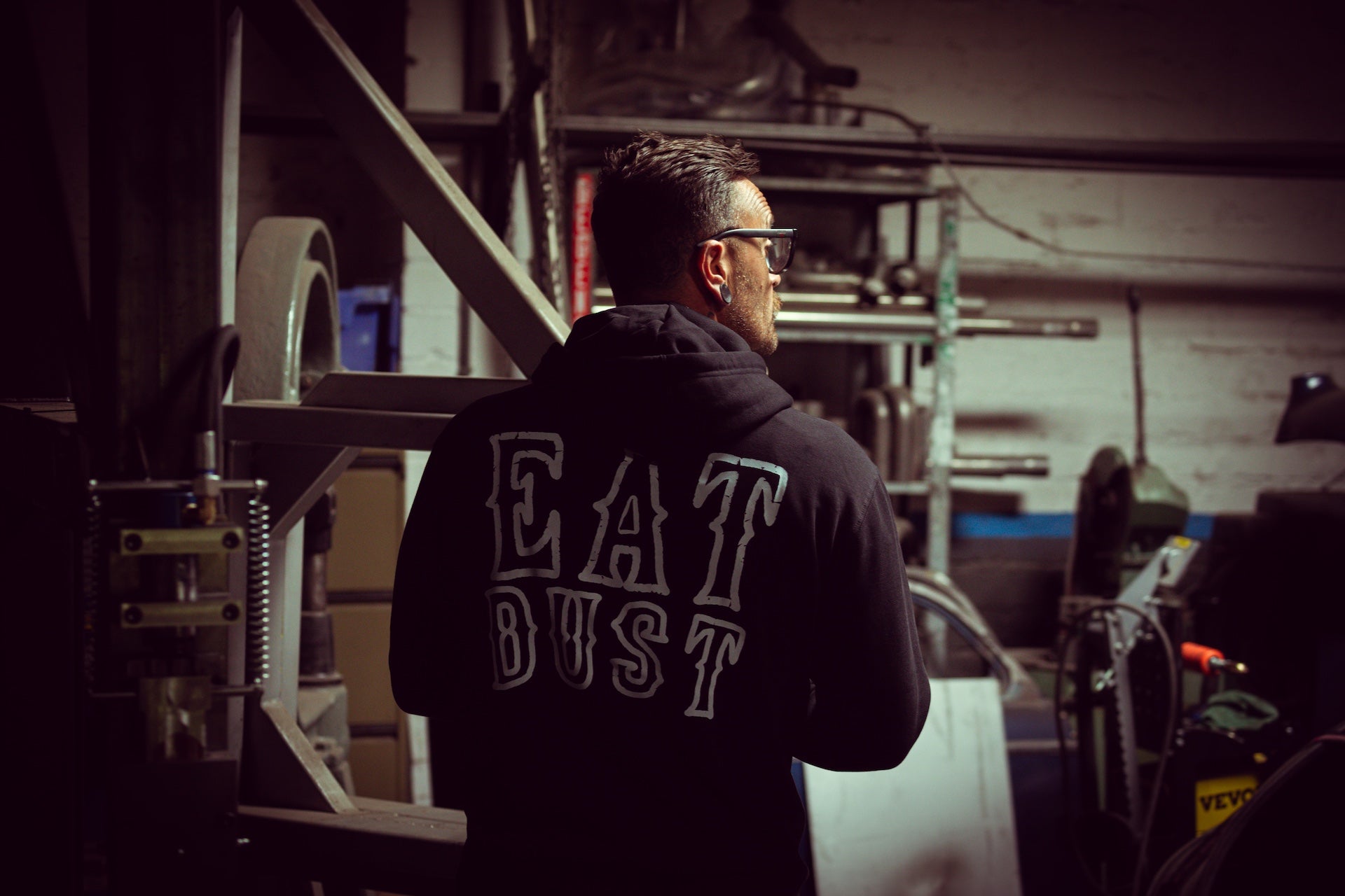 Person wearing a black hoodie with 'EAT DUST' text in a workshop setting
