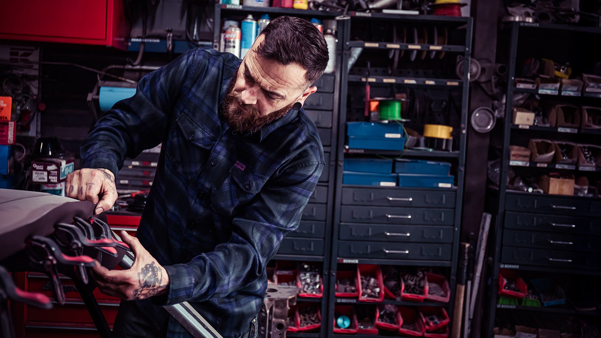 man fixing a car wearing the black and purple kiss the sky flannel 