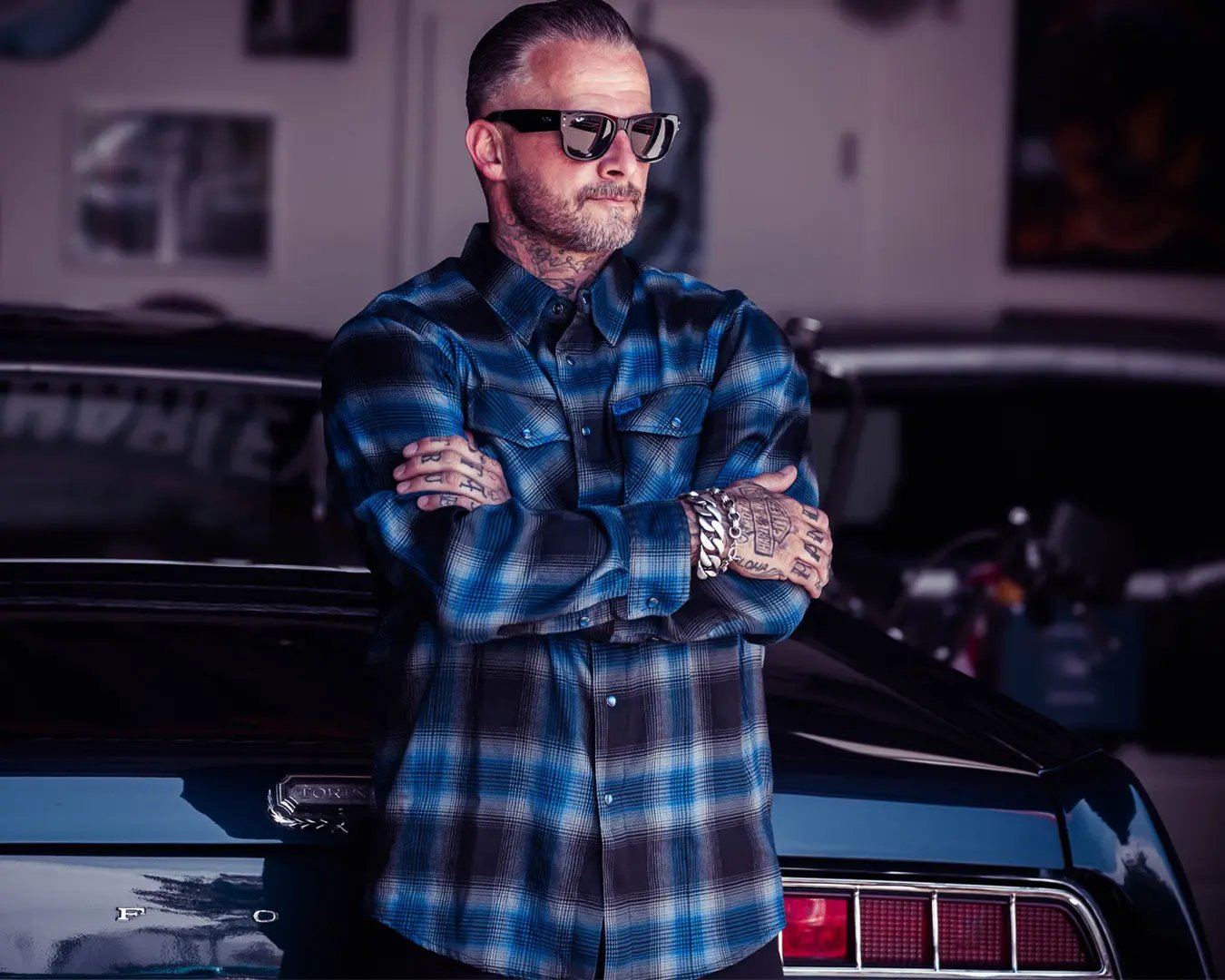 a man standing in an industrial setting wearing a blue and black flannel shirt - The Nailhead Flannel by Greasy Hands Society