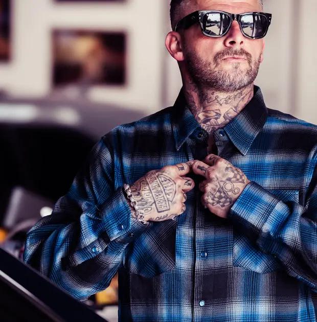 a man wearing a blue black and while plaid flannel shirt and sunglasses in a workshop setting - The Nailhead Flannel by Greasy Hands Society