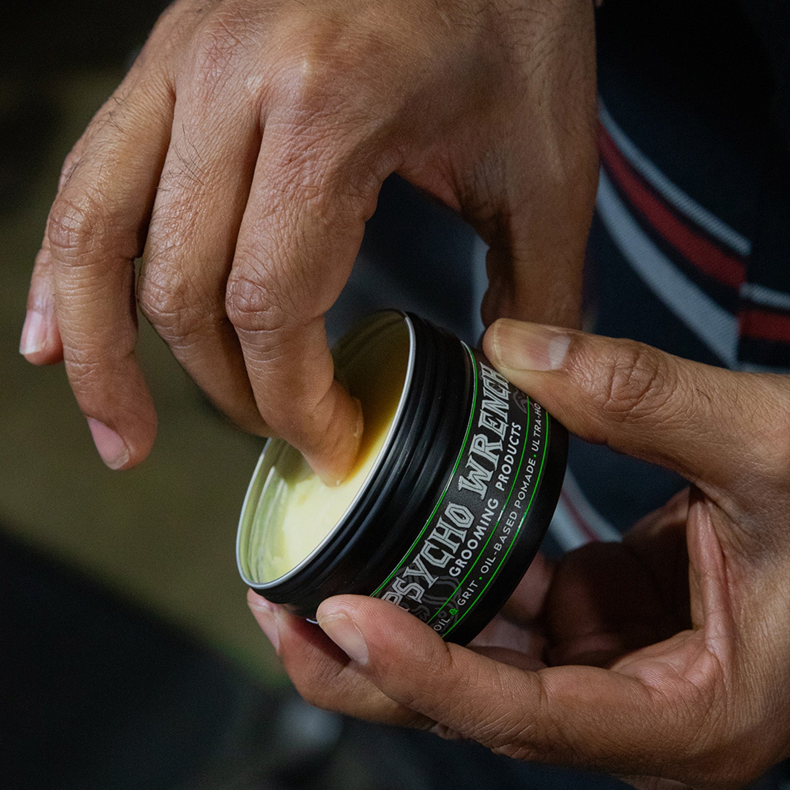 Person holding a container of 'Psycho Wrench' pomade product with a focus on the brand name - Psycho Wrench grooming product clay-based pomade