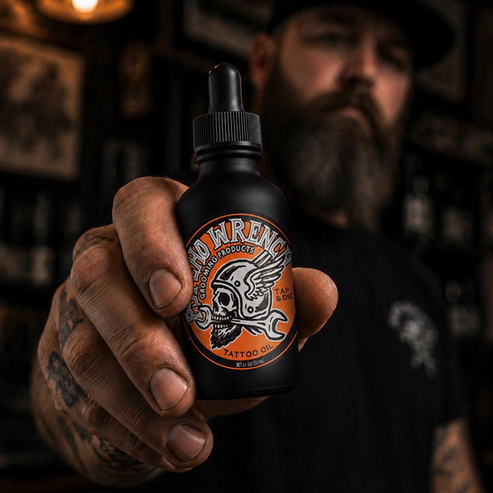 Person holding a bottle of 'Psycho Wrench' tattoo oil with a dark background - Psycho Wrench grooming product - tattoo oil