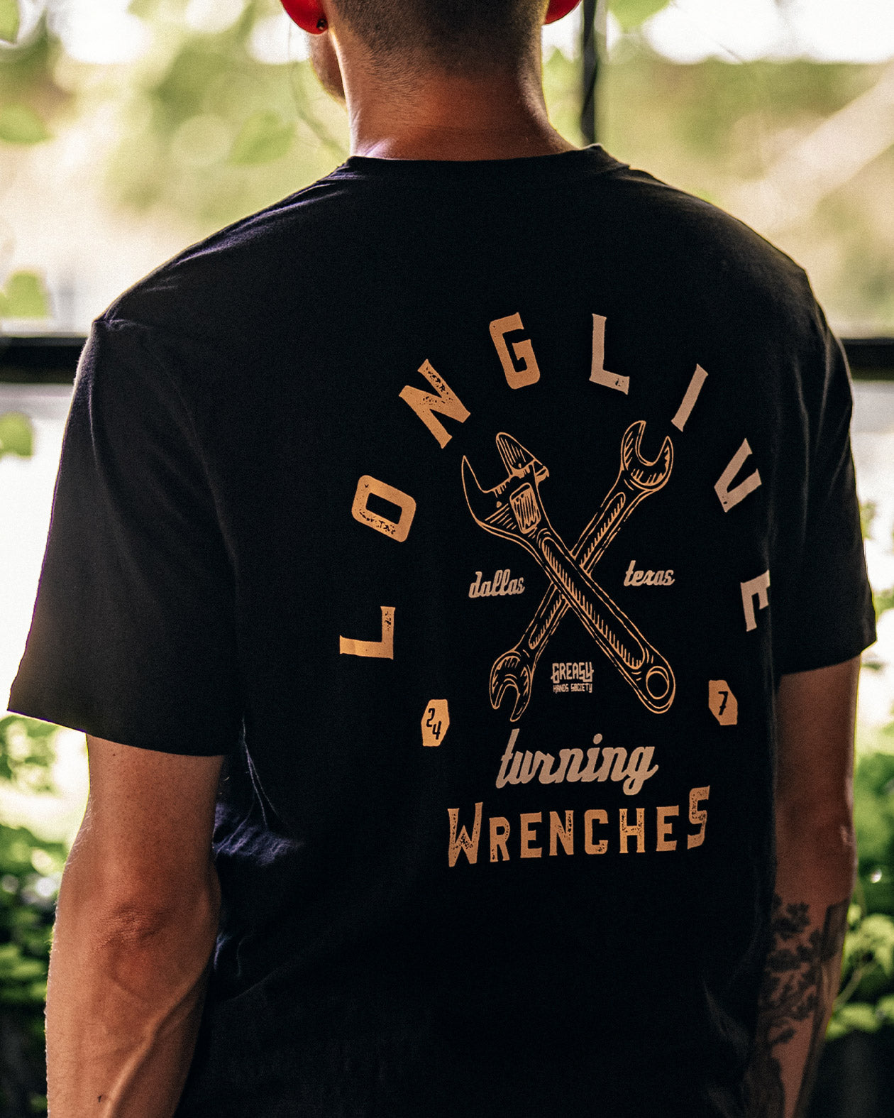 Person wearing a black t-shirt with a graphic design on the back, standing outdoors - Turning Wrenches graphic tee by Greasy Hands Society