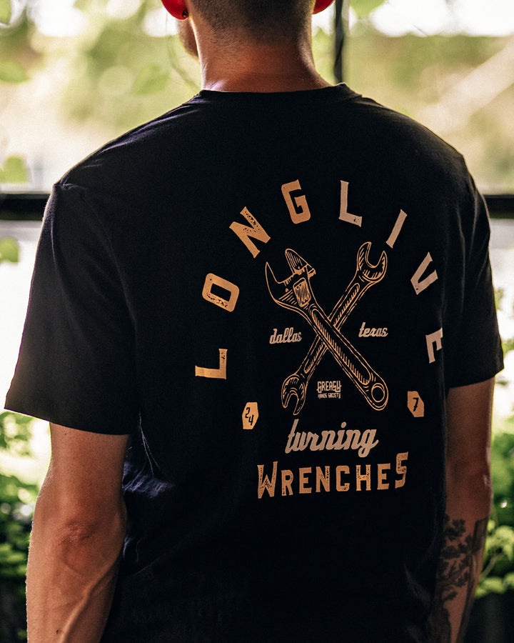 Person wearing a black t-shirt with a graphic design on the back, standing outdoors - Long Live Turning Wrenches graphic tee by Greasy Hands Society