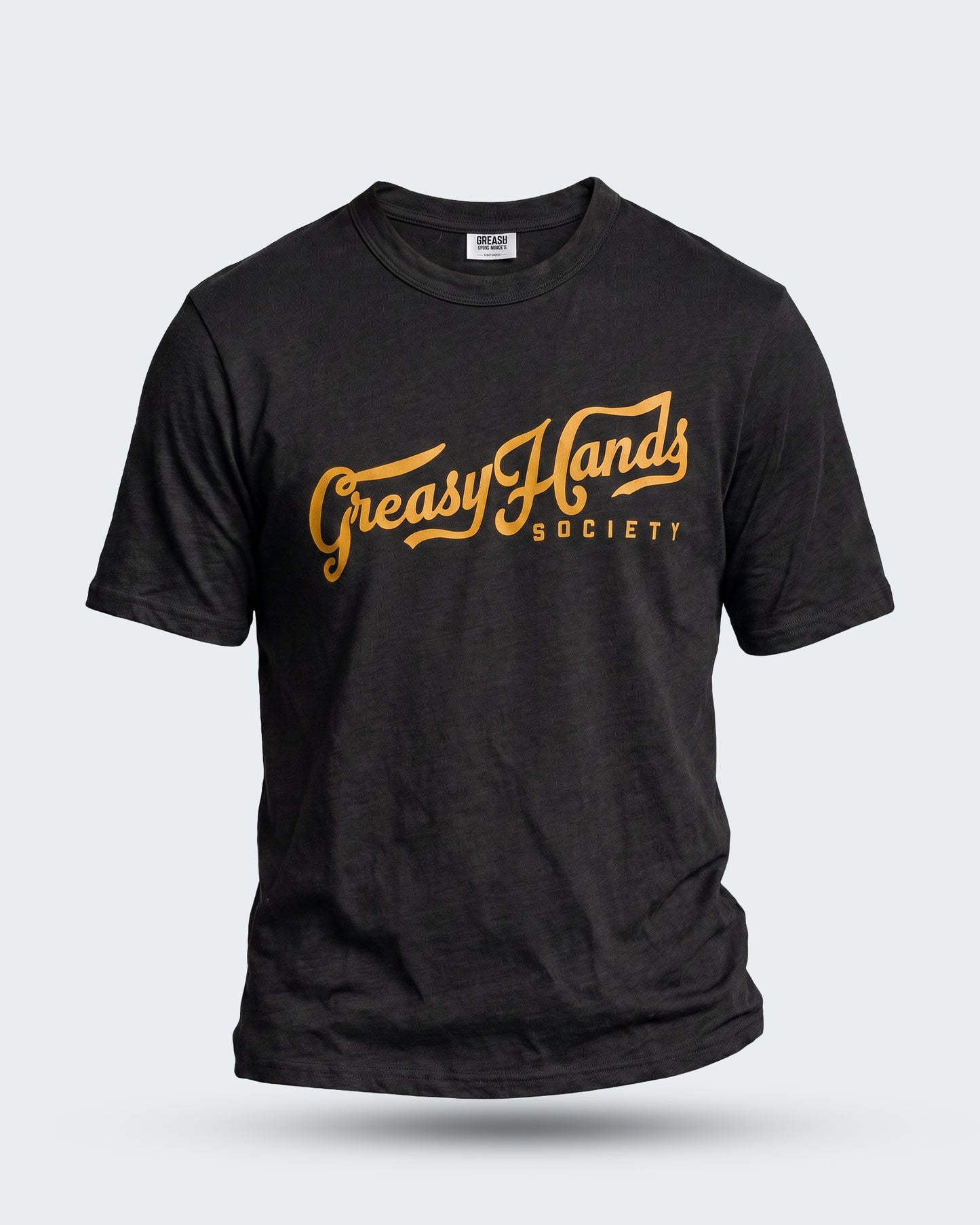A black short-sleeve t-shirt with a distressed graphic on the chest reading 'Greasy Hands Society' in a golden-yellow cursive font, displayed against a light gray background - Greasy Hands Society Script graphic tee by Greasy Hands Society 