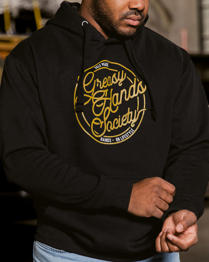 Person wearing a black hoodie with yellow text design - Self Made Hoodie by Greasy Hands Society