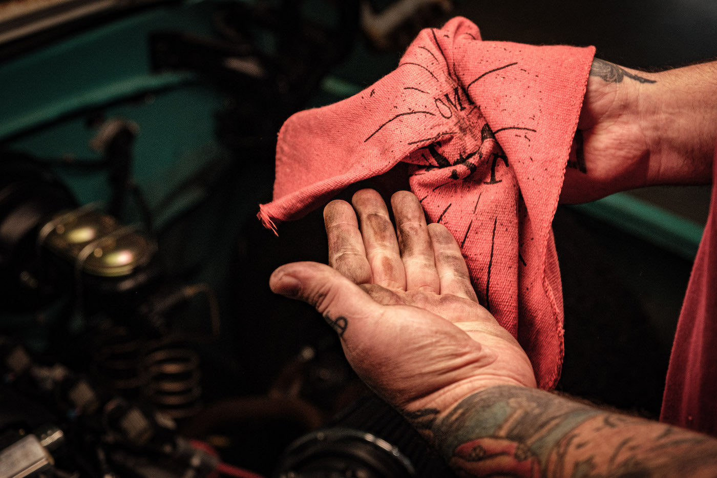 Hand with tattoos holding a red shop rag over a mechanical engine background
